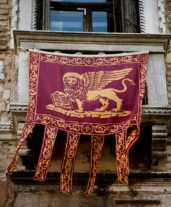 A decorative Lion of St. Mark banner hangs from a Venetian balcony, showcasing historical architecture.